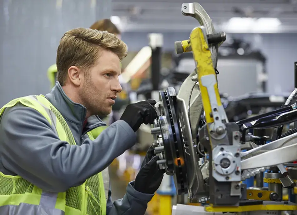 Young man working on a car chassis at an automobile manufacturing plant in a high-vis jacket