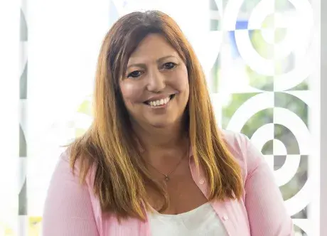 Chris Rhodes smiling at the camera wearing a pink top over a white t-shirt