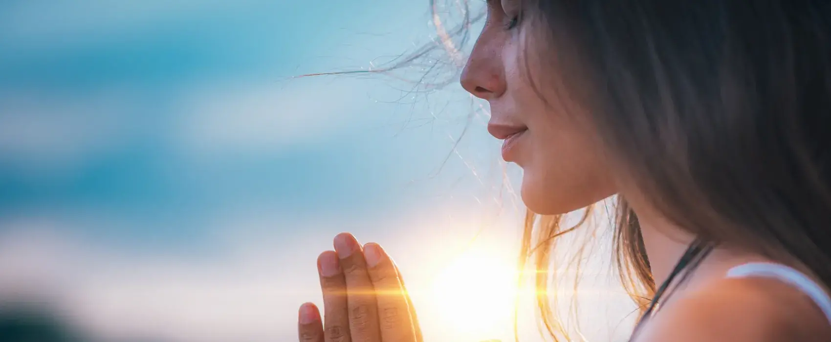 Young woman outside side profile photo eyes closed and hands in prayer with sun in background