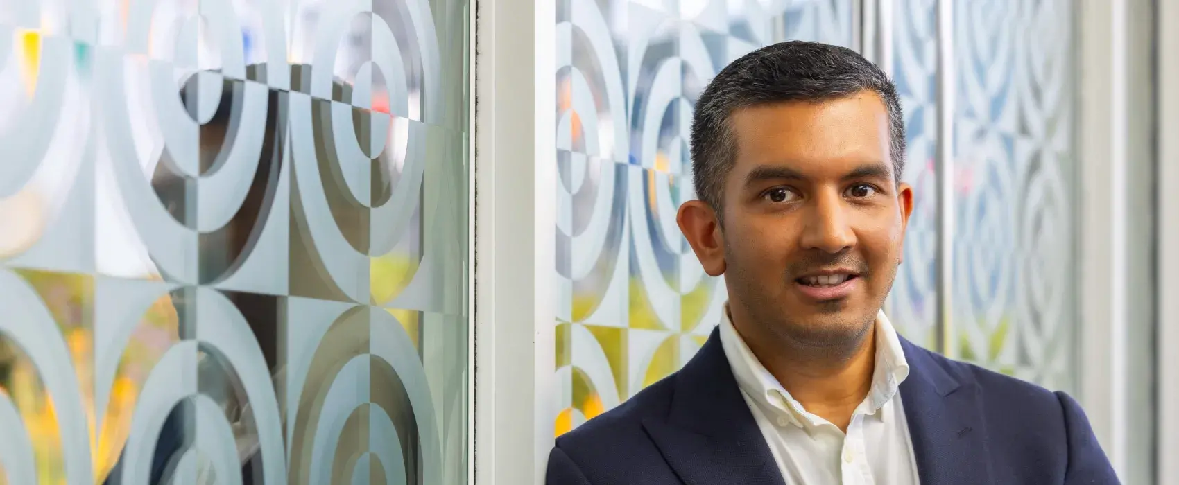 A head and shoulders photo of a male doctor leaning against a textured white and transparent glass wall