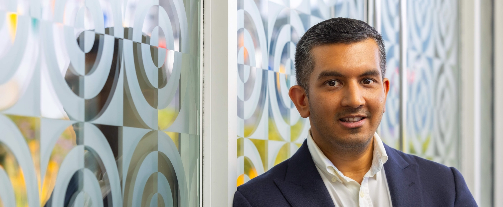 A head and shoulders photo of a male doctor leaning against a textured white and transparent glass wall
