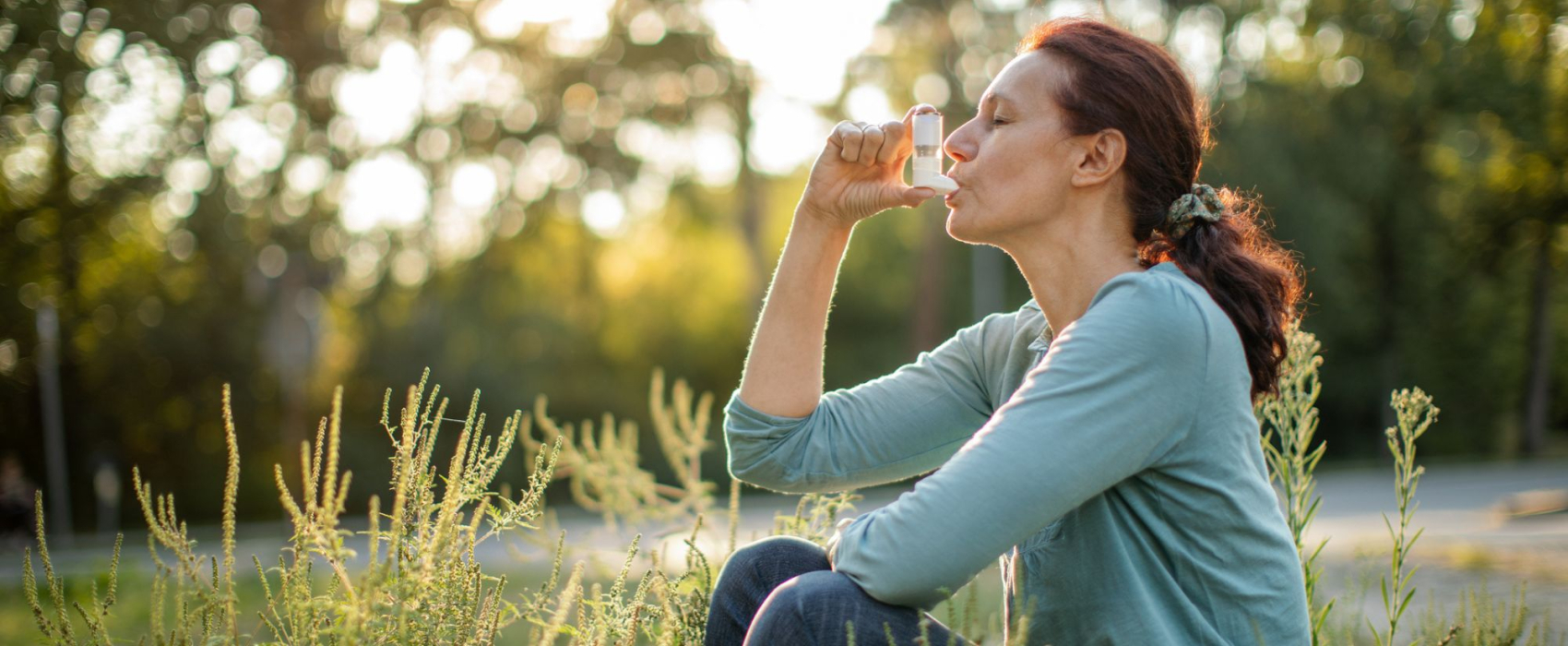 Woman sitting in field using asthma inhaler