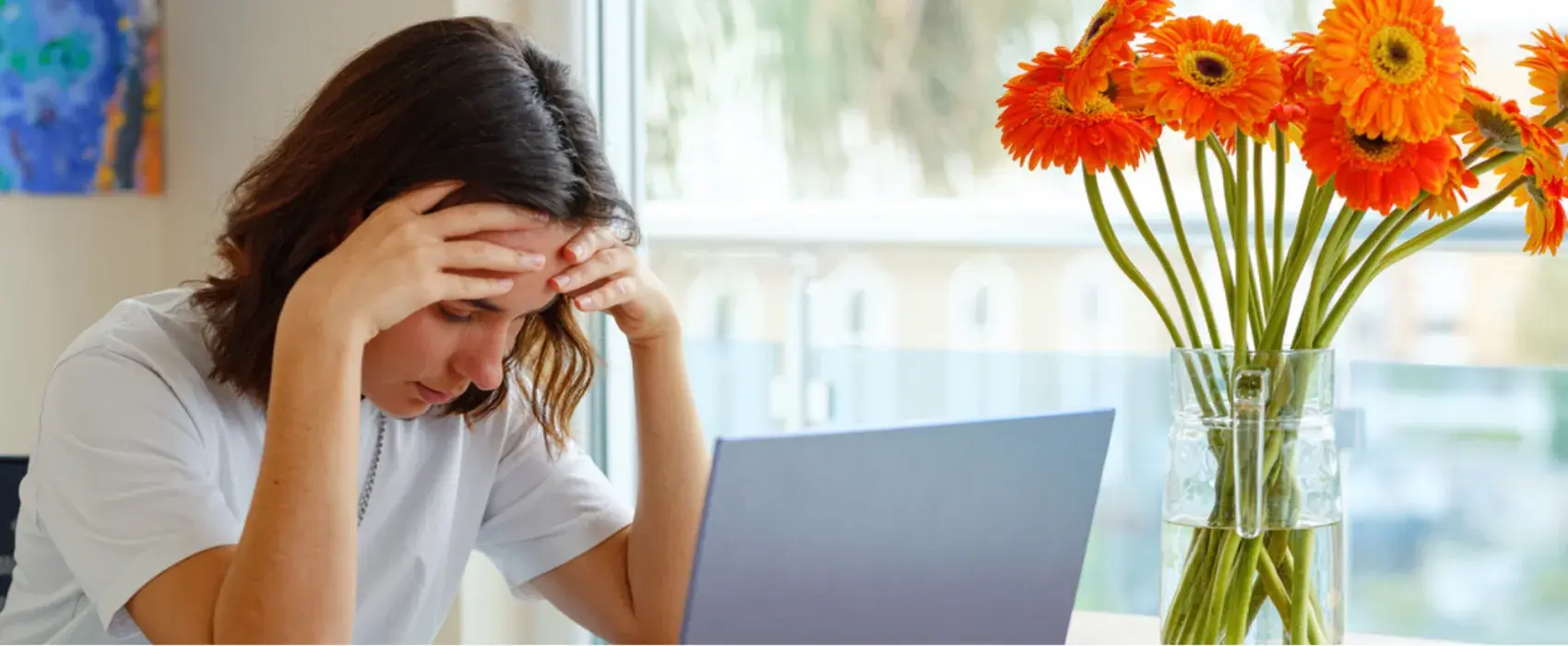 Woman holding head in hands whilst looking at a laptop