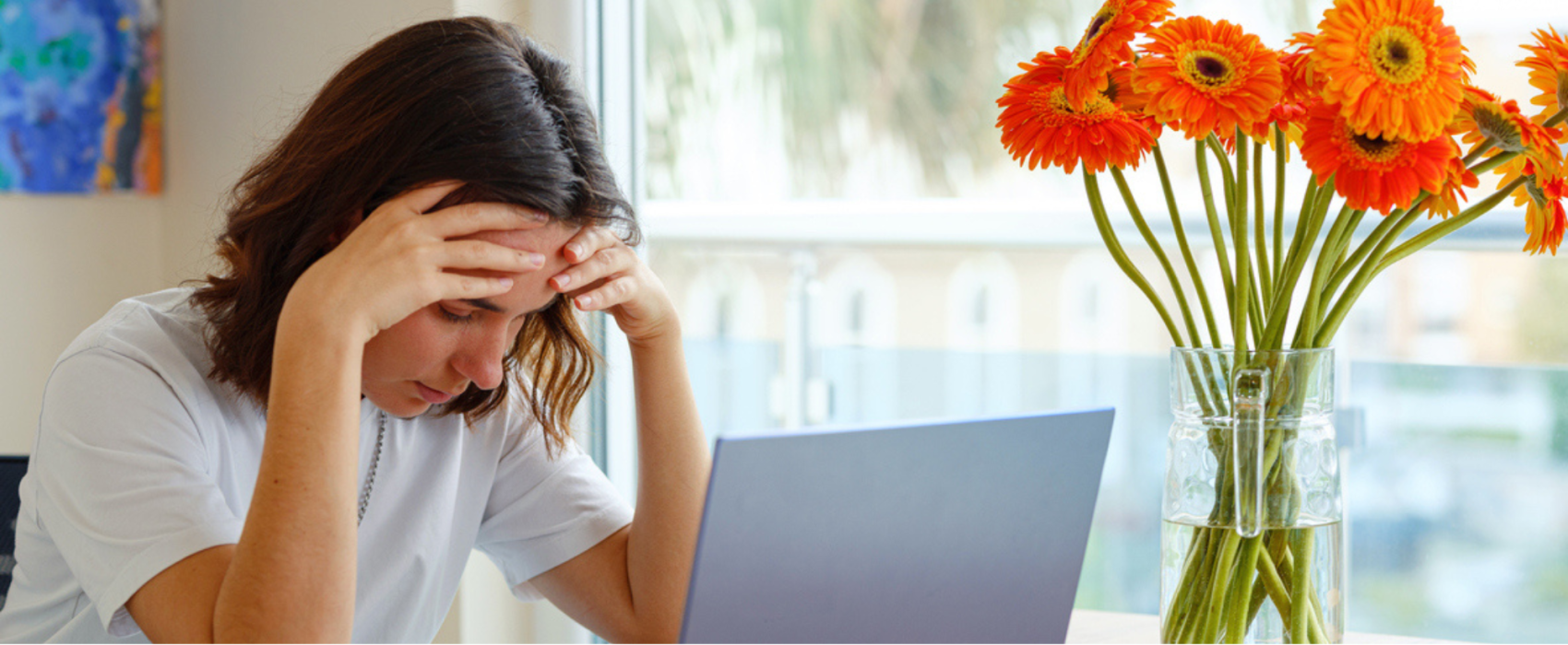 Woman holding head in hands whilst looking at a laptop