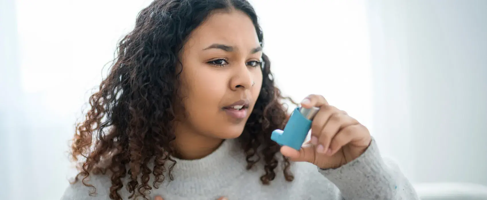 Woman using an inhaler with hand on chest