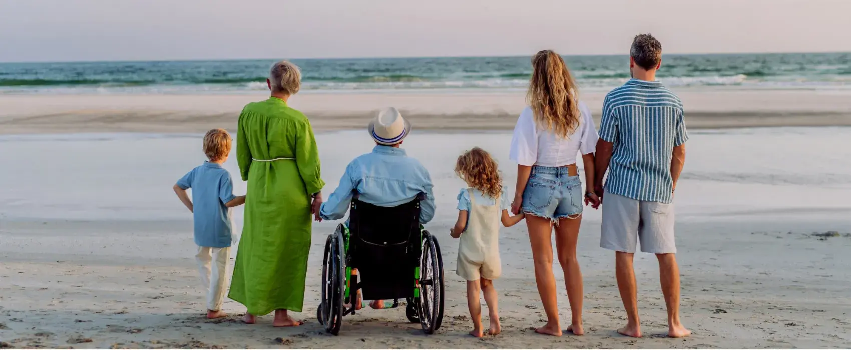A family of three generations standing on the beach looking out into the water