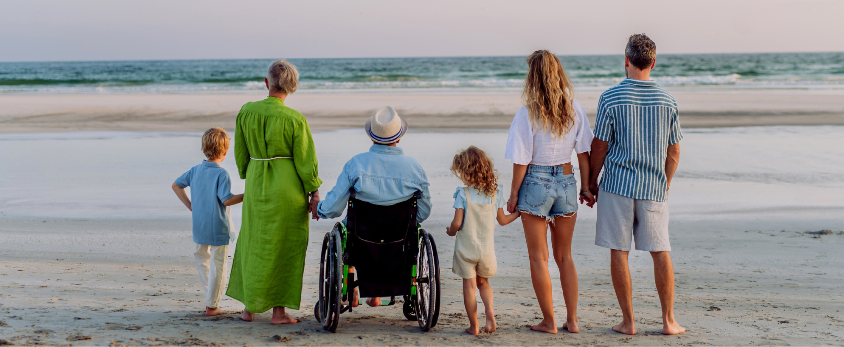 A family of three generations standing on the beach looking out into the water