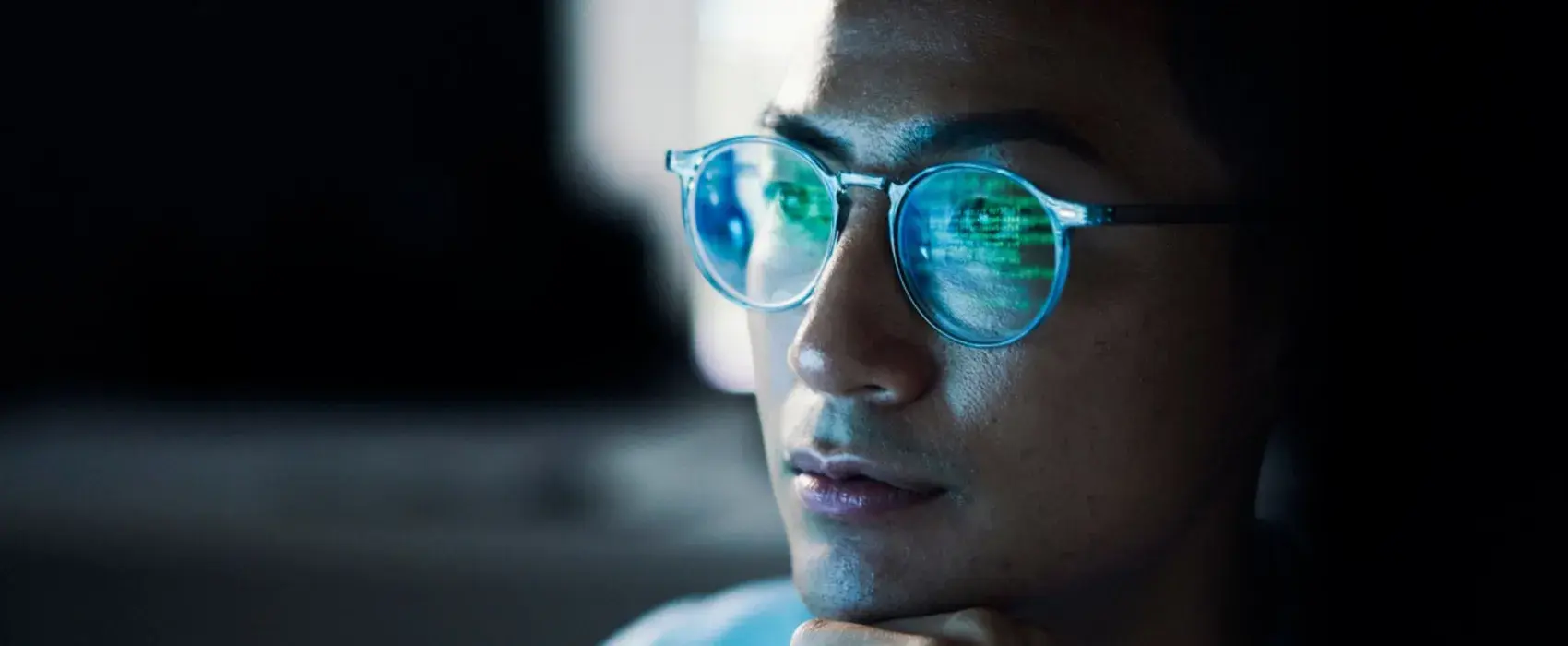 A man in a dark room with computer screen reflecting in glasses