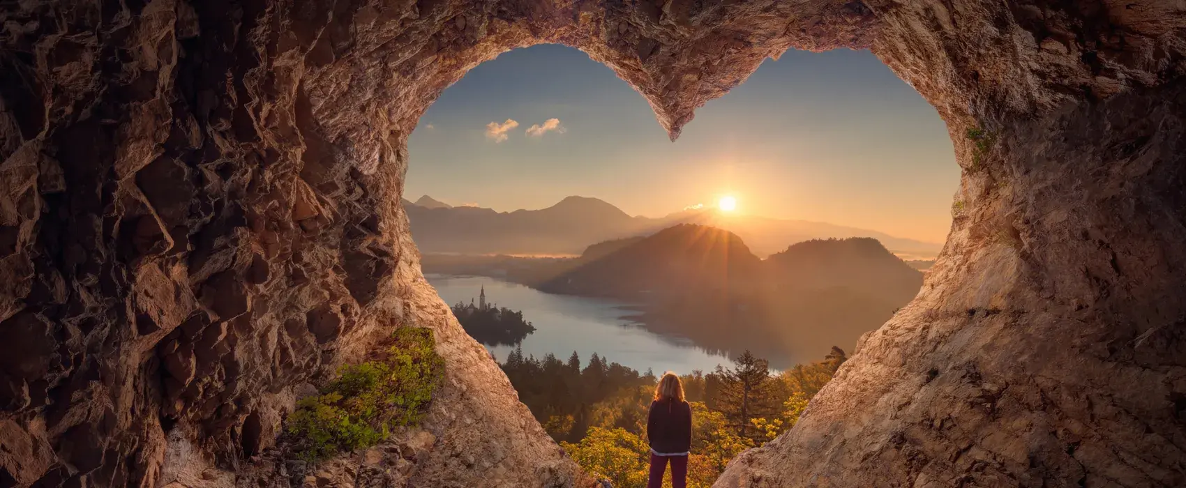 woman standing in a heart shaped cave looking out at a sunset