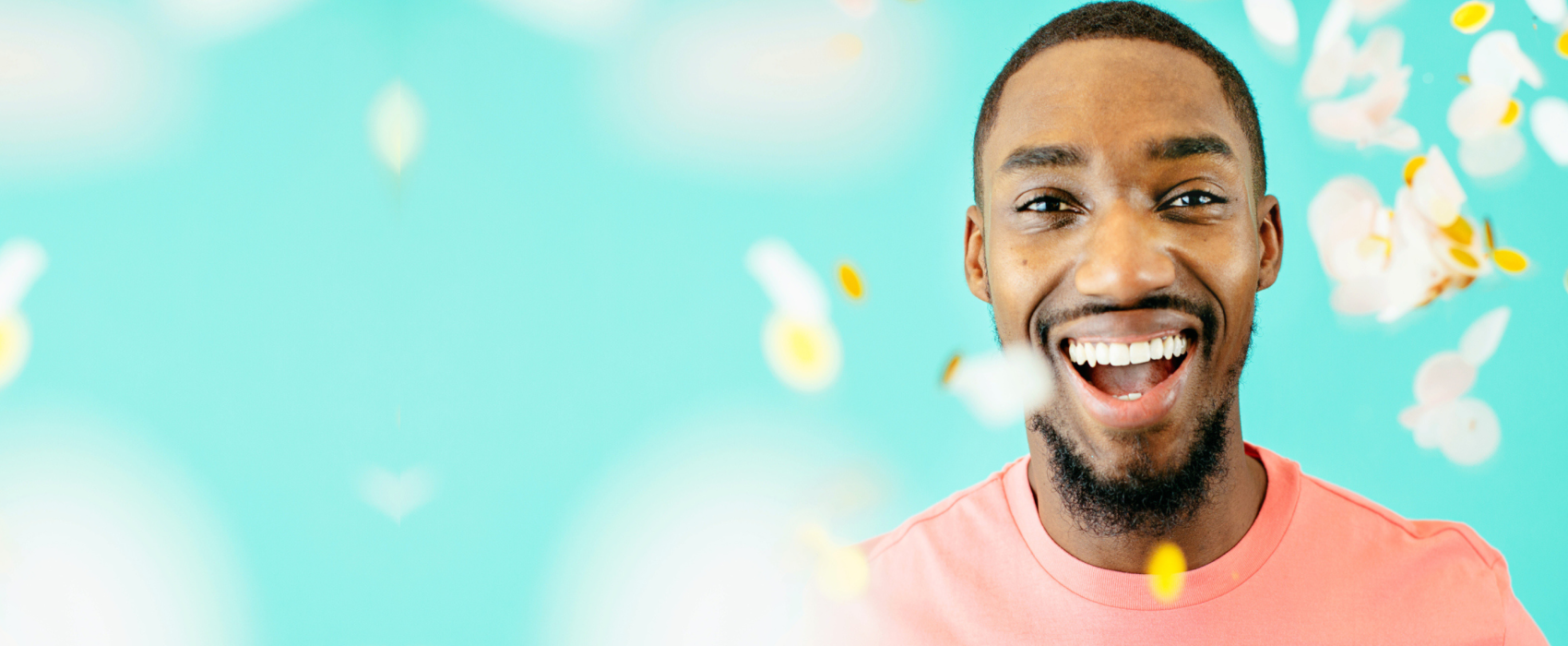 Young Black man laughing at the camera wearing a pink t-shirt with gold and white confetti in the air around him