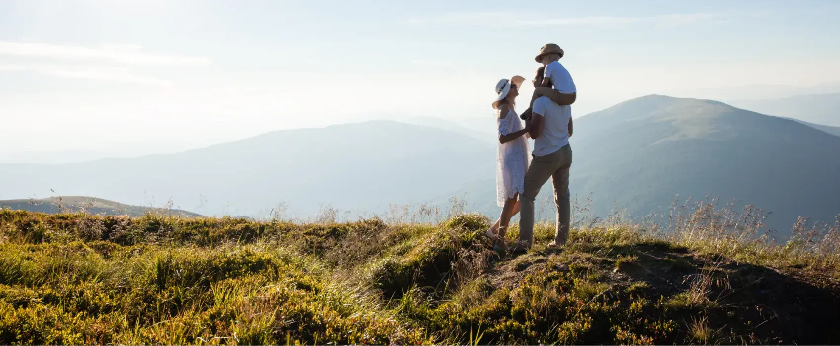 A woman standing next to a man with a child sitting on his shoulders looking out over a hilly view
