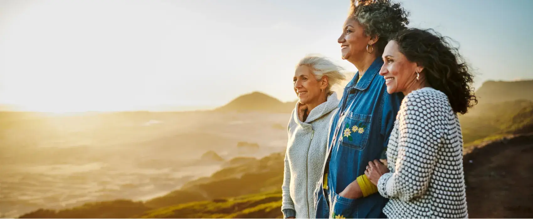 Smiling mature friends standing arm in arm by a scenic coast during a road trip stock photo