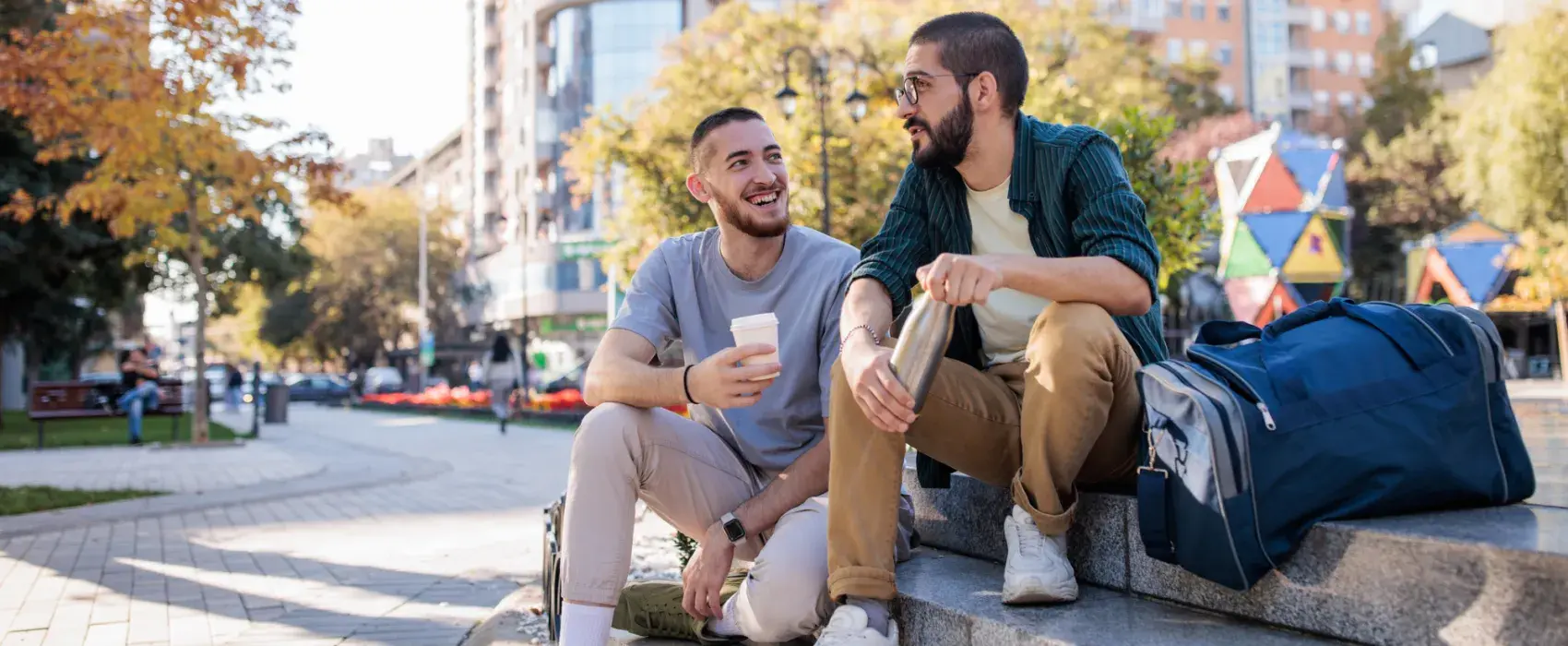 Two male friends talking while sitting on concrete steps in the park in city.