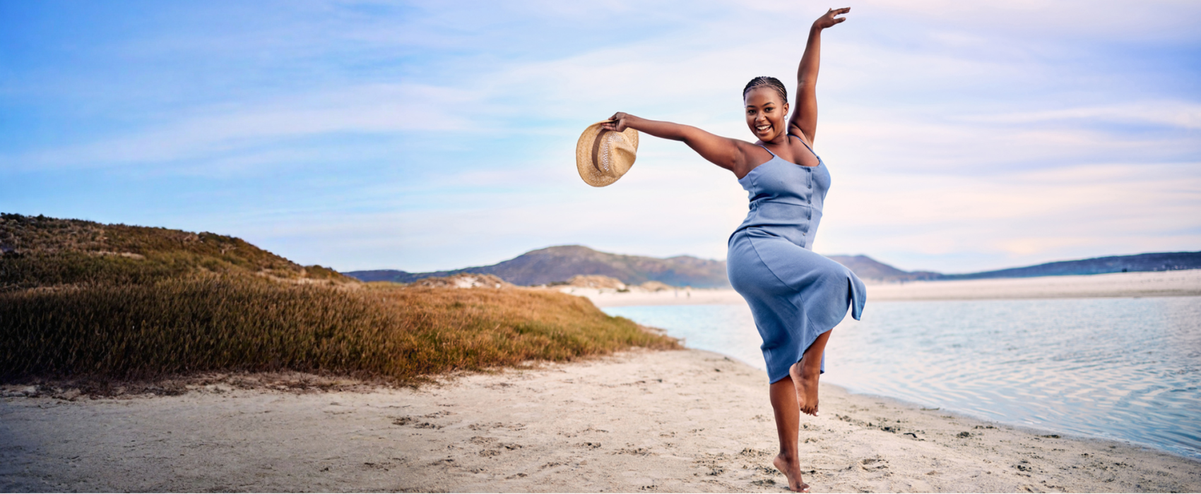 Women in a light blue dress dancing on sandy beach by the sea
