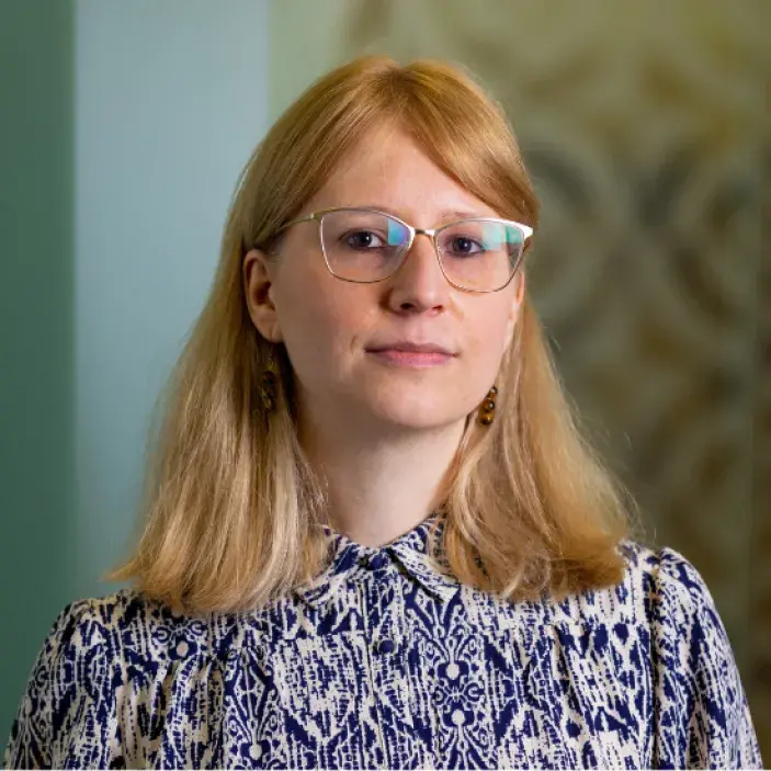 Blonde woman with glasses on and a patterned blue and white blouse