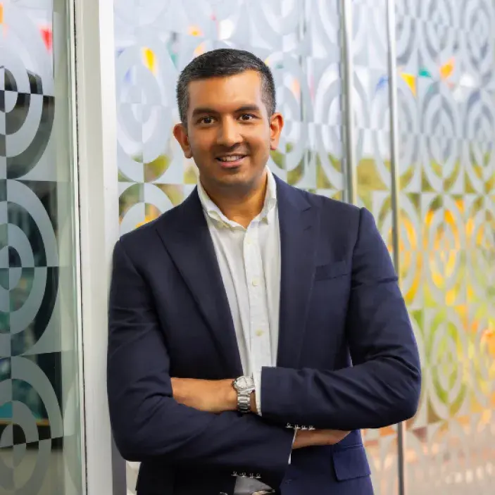 Young dark-haired man in a dark suit crossing his arms and smiling