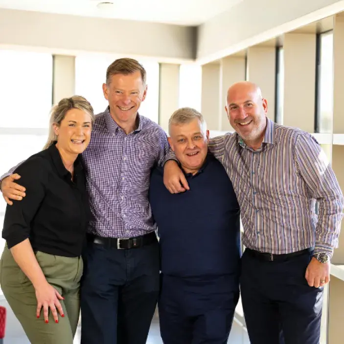 Group of four men and women standing next to each other, arms around each other and laughing