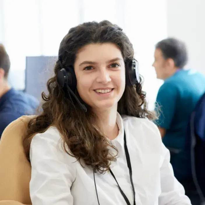 Woman with curly dark hair and a headset on looking at the camera 