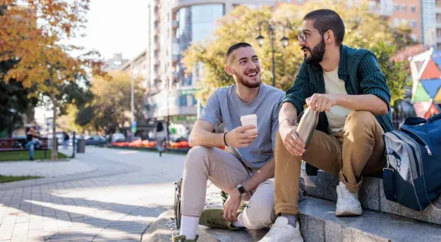 Two male friends talking while sitting on concrete steps in the park in city.
