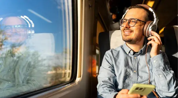 A man wearing headphones whilst looking out train window